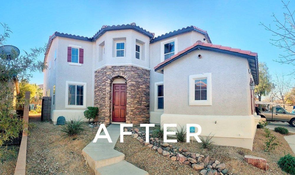 A two-story stucco house after renovations. Tan and white exterior with stone accents and red door.