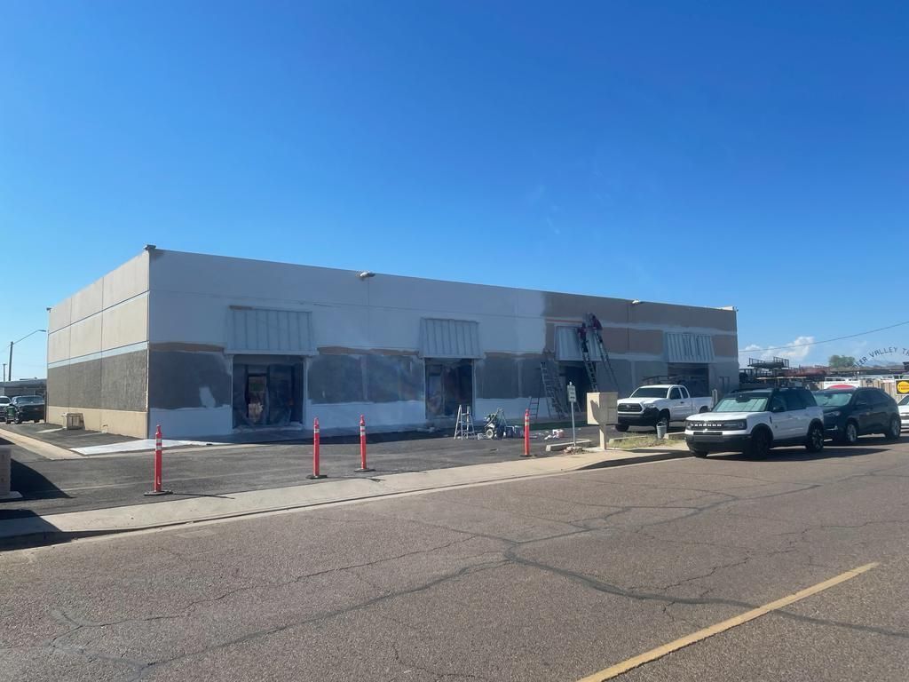 Exterior of a building under construction, grey and white colors. Construction equipment and vehicles present.