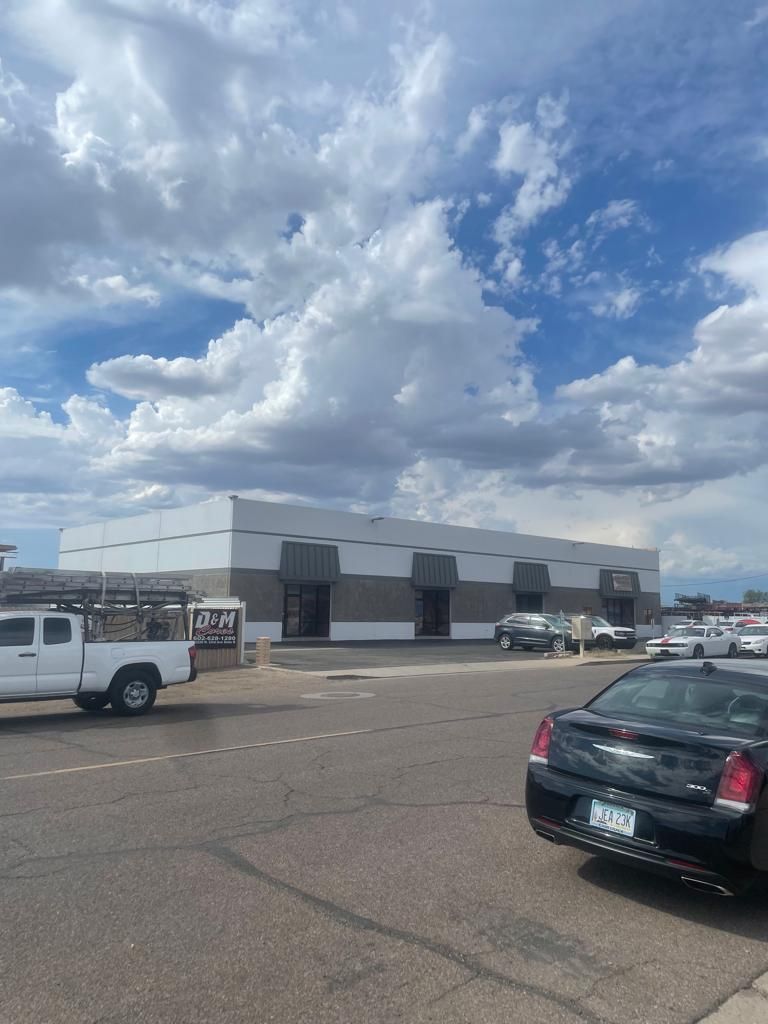 Exterior of a commercial building with a blue sky and parked vehicles in a parking lot.