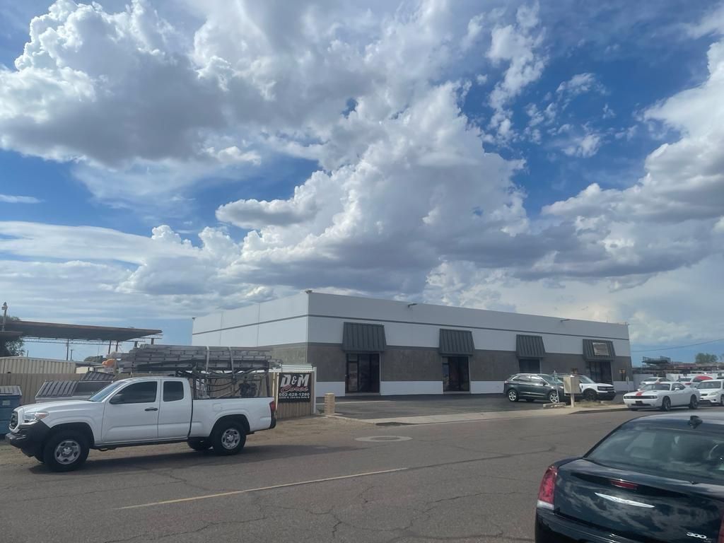 White building with a dark roof and several parked vehicles under a cloudy sky.