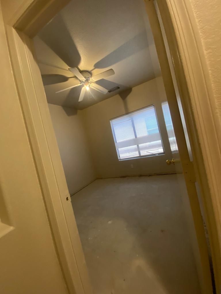 Empty room with a ceiling fan, a window with blinds, and light-colored walls.