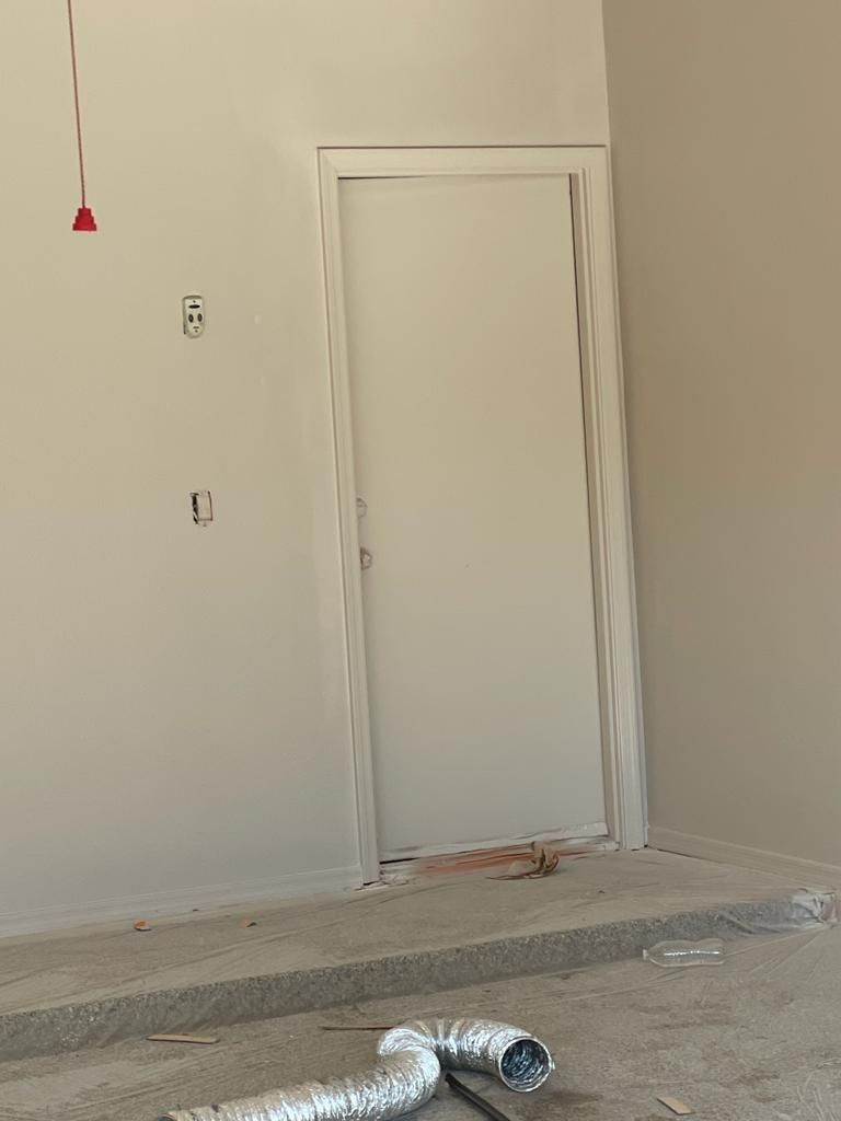 White door in unfinished room with exposed wiring and concrete flooring.