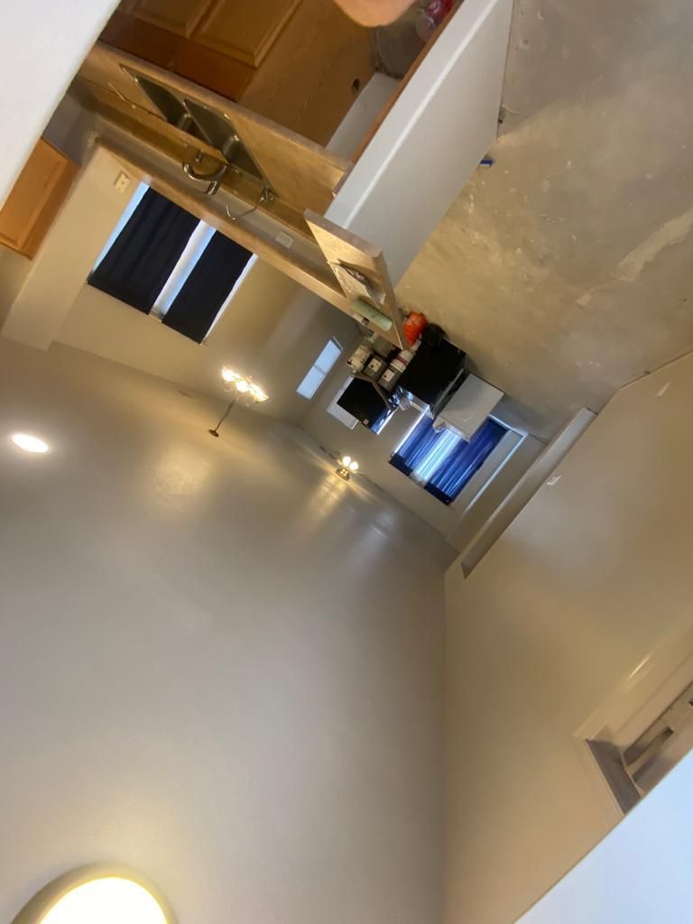 Long, narrow kitchen/living space with high ceilings and light-colored walls. Kitchen appliances visible.