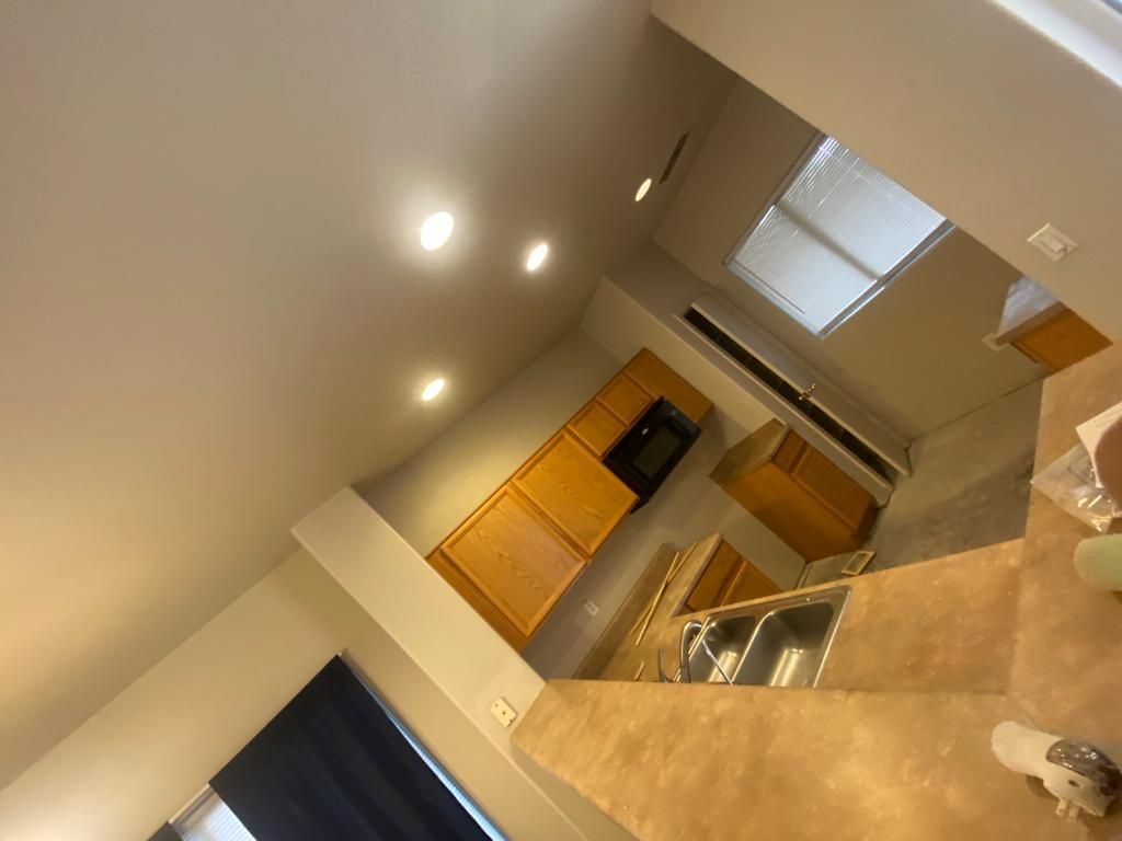 Kitchen with light wood cabinets, built-in microwave, sink, and high ceiling.