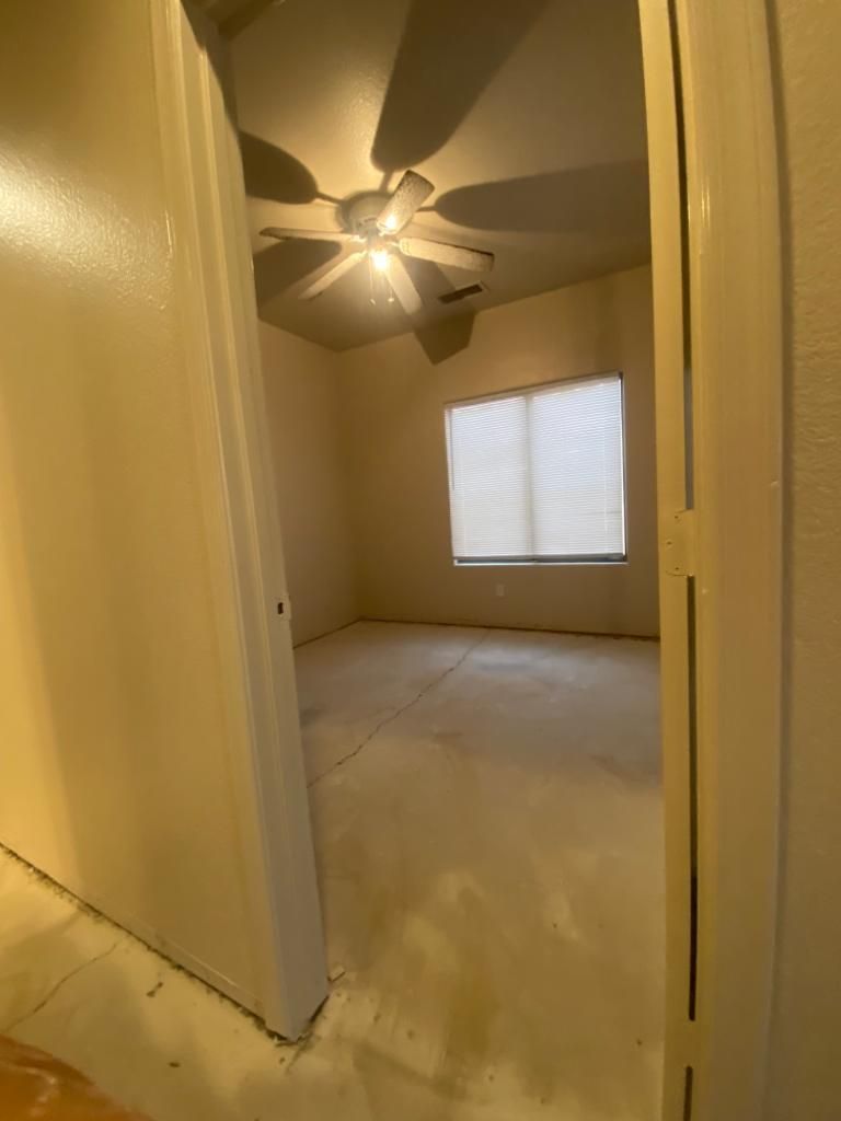 Empty room with beige walls and flooring. Ceiling fan with lights, window with closed blinds.