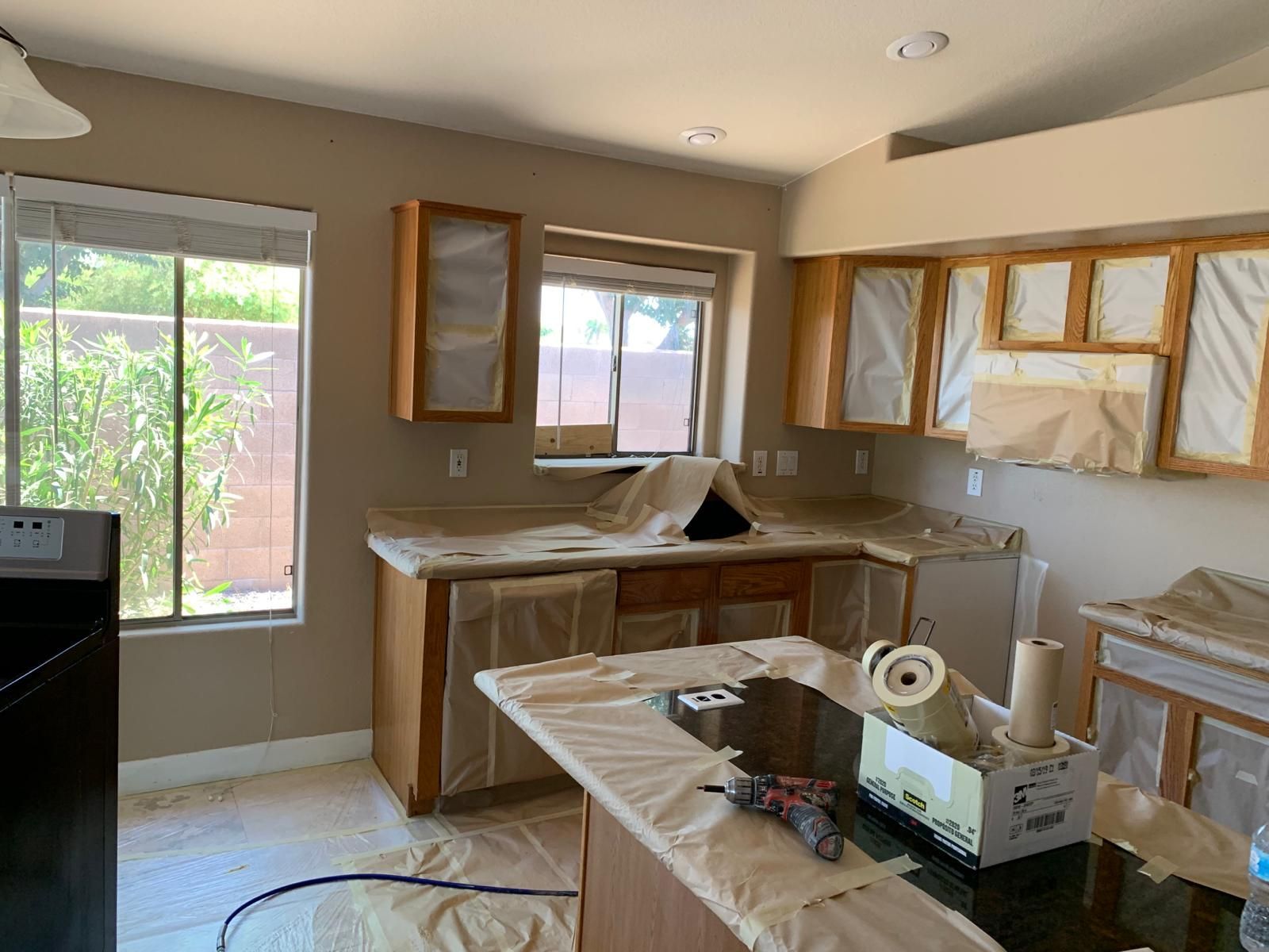 Kitchen with cabinets covered in paper for painting; counters and island also covered; window.