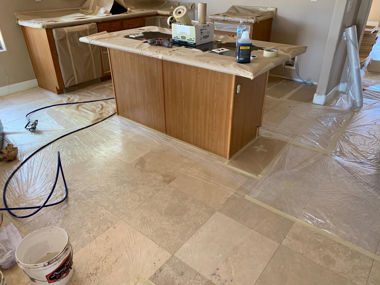 Kitchen under renovation with tile floor, cabinets covered in plastic, island workspace, and tools present.