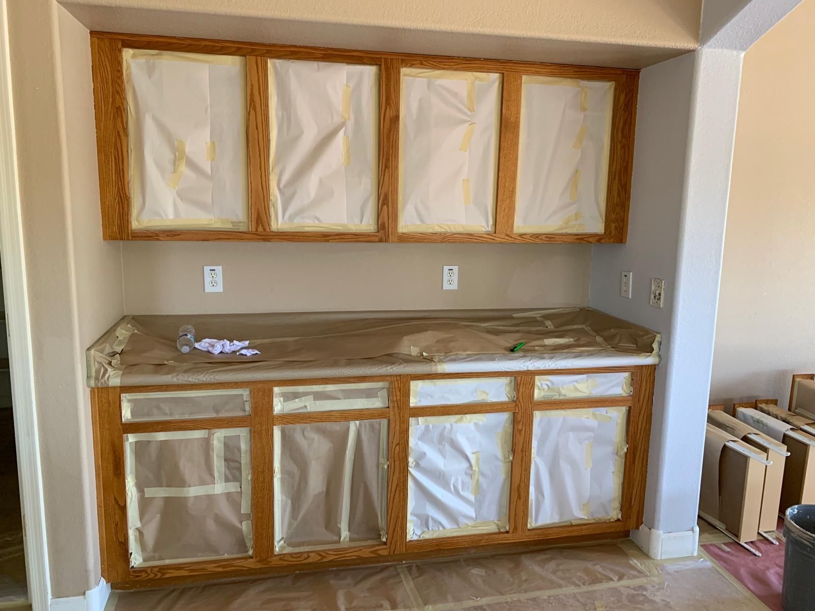 Kitchen cabinets taped for painting; light wood frames with plastic covering.