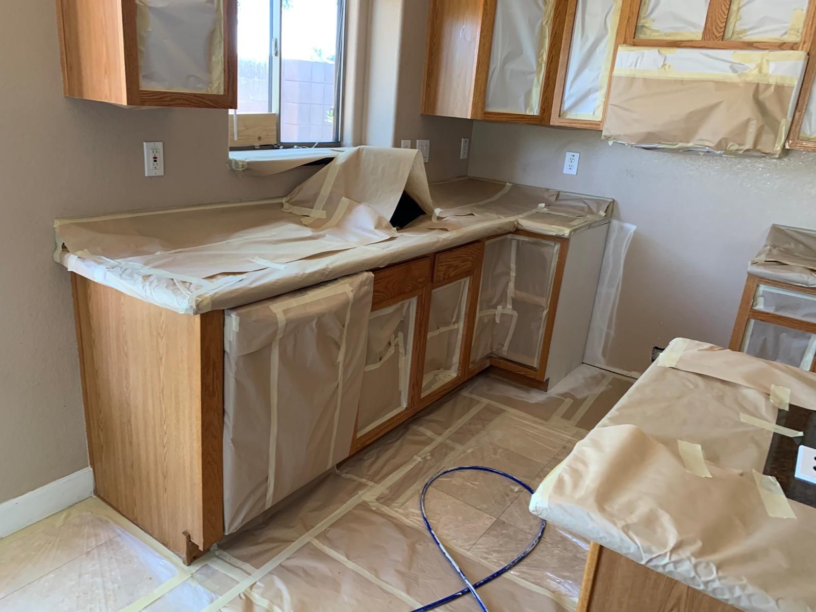 Kitchen cabinets and countertops covered in protective paper, preparing for painting.