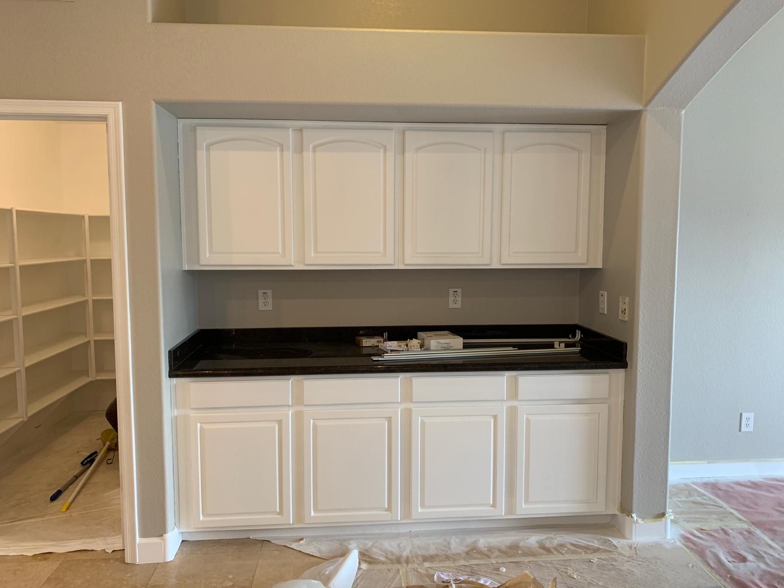 White cabinets with a black countertop in a room under construction, with a pantry to the left.
