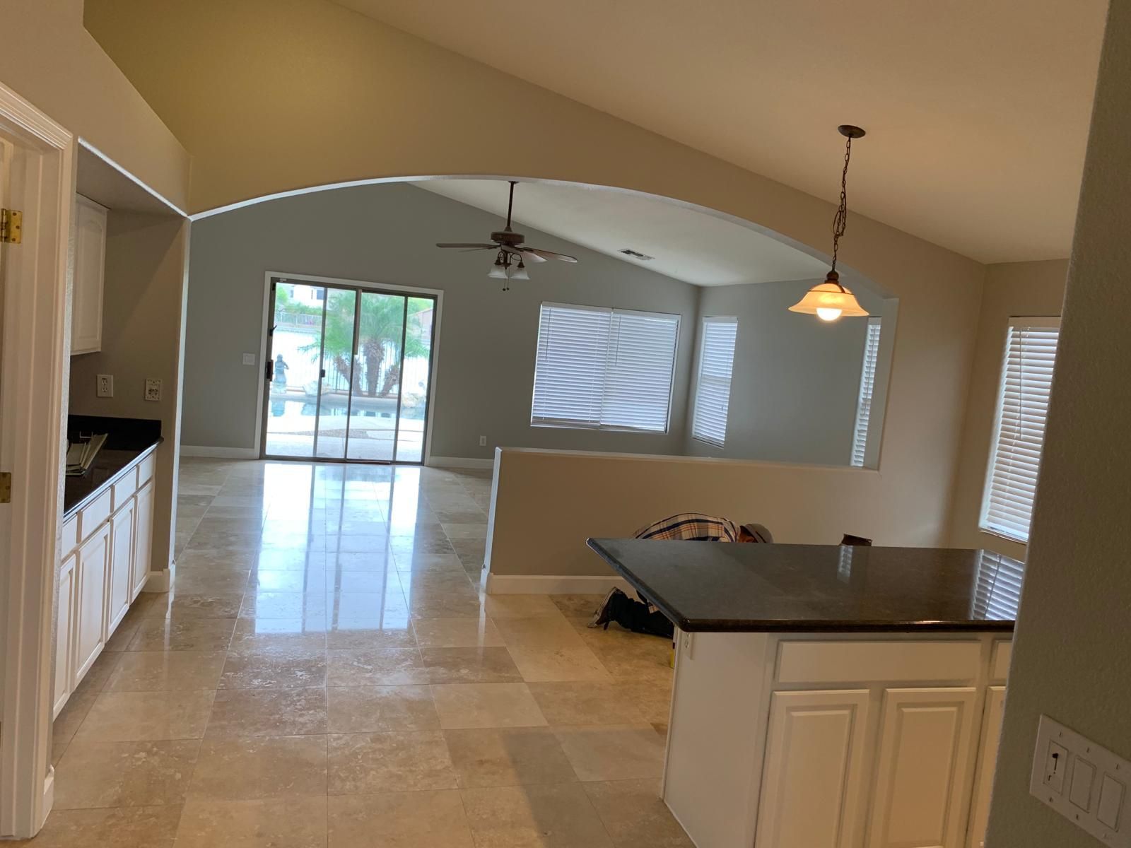 Open-concept living space with kitchen, archway, tile floor, and sliding glass door to backyard. Beige walls and white cabinets.
