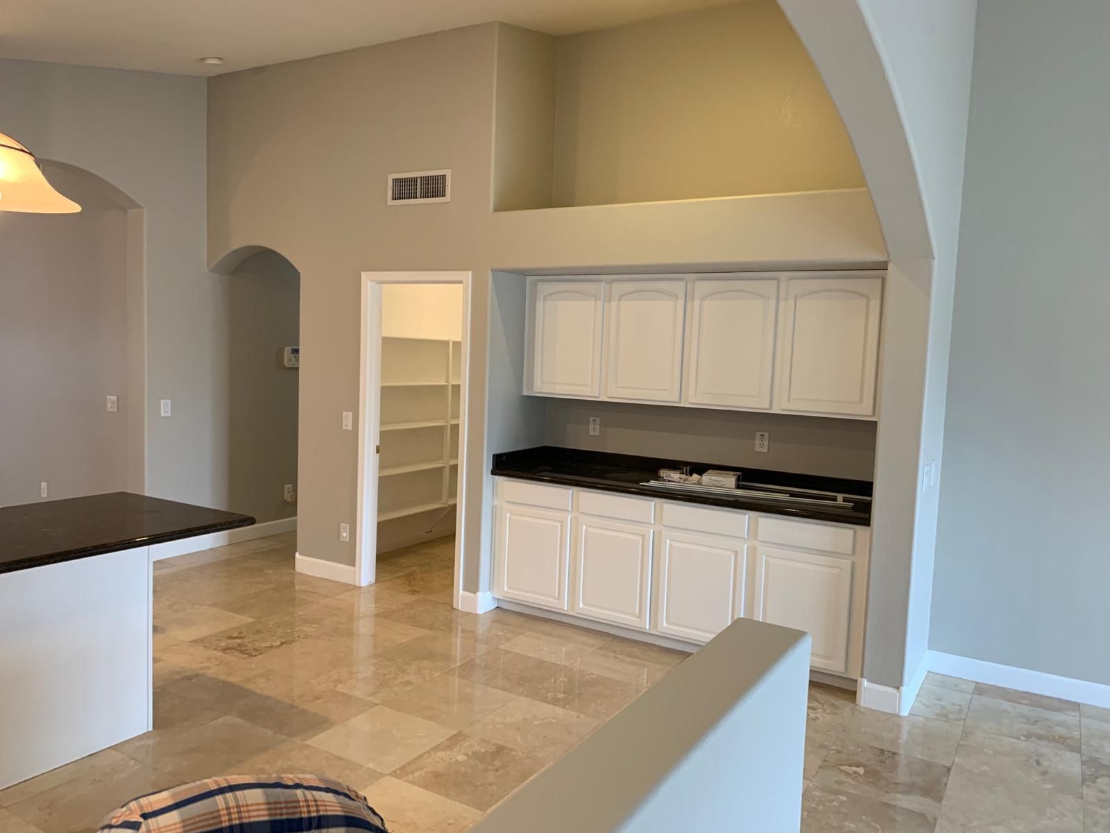 Interior view of a kitchen with white cabinets, pantry, and a black countertop. Gray walls and tiled floor.
