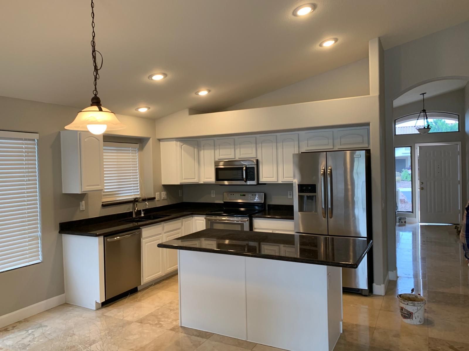 A well-lit kitchen with white cabinets, stainless steel appliances, and a black countertop island.