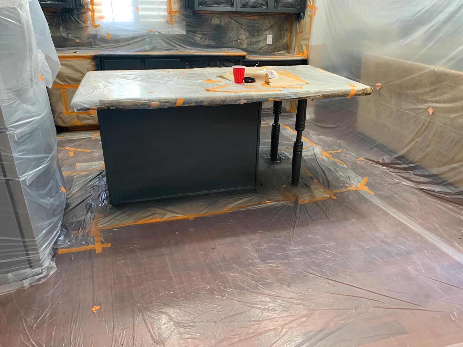 Kitchen renovation, island with concrete countertop, covered in plastic, taped off flooring.