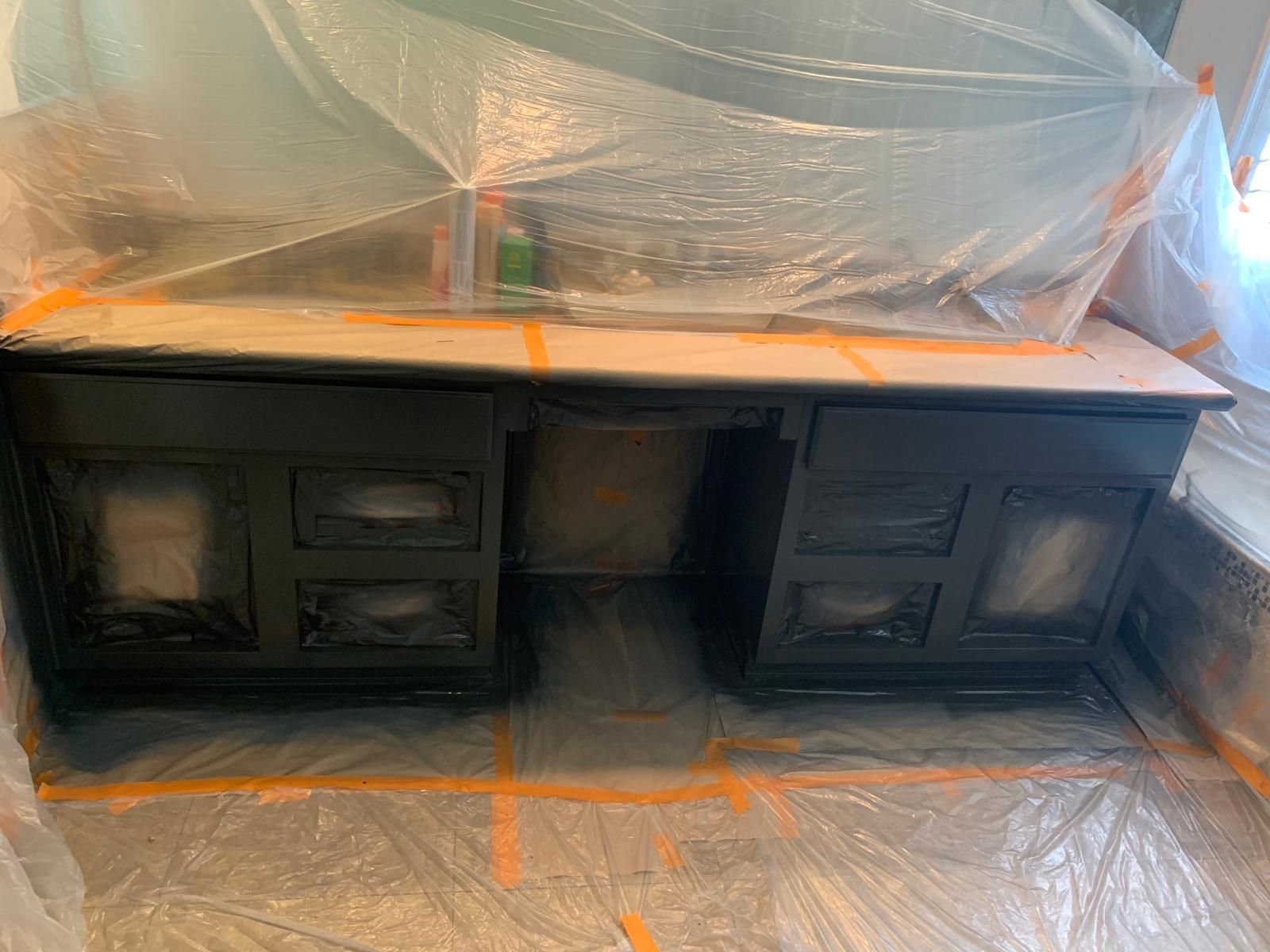 Black painted vanity cabinet covered in plastic sheeting for painting, taped to the floor.