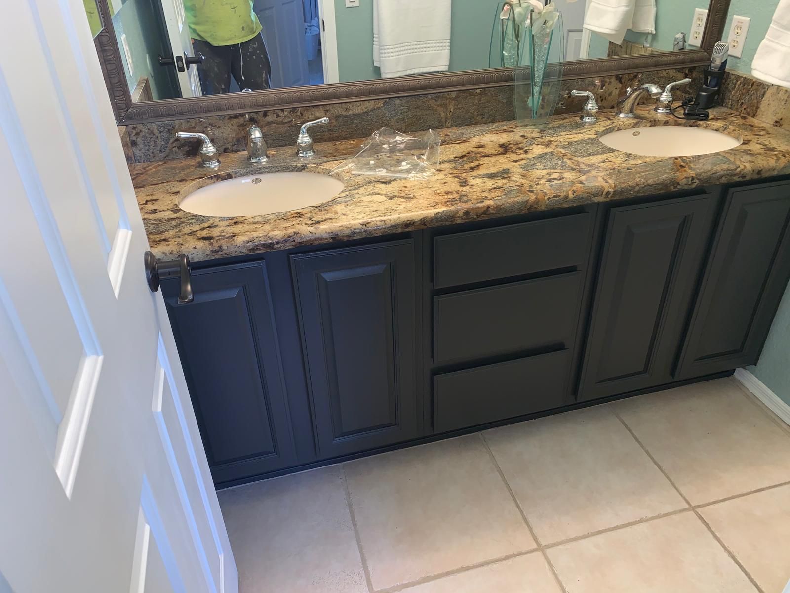 Bathroom vanity with dark cabinets, two sinks, granite countertop, mirror, and white door.