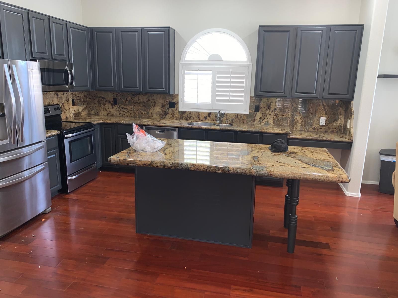Kitchen with dark gray cabinets, granite countertops, and wood flooring; stainless steel appliances.