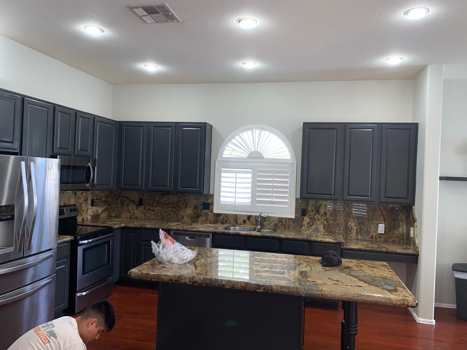 Kitchen with dark cabinets, granite countertops, and island; a person works in the foreground.