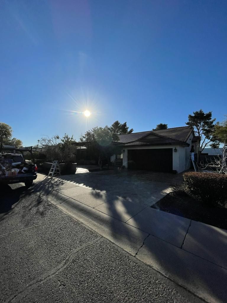 Sunlit house with dark garage door, short bushes, and a parked vehicle on the left.