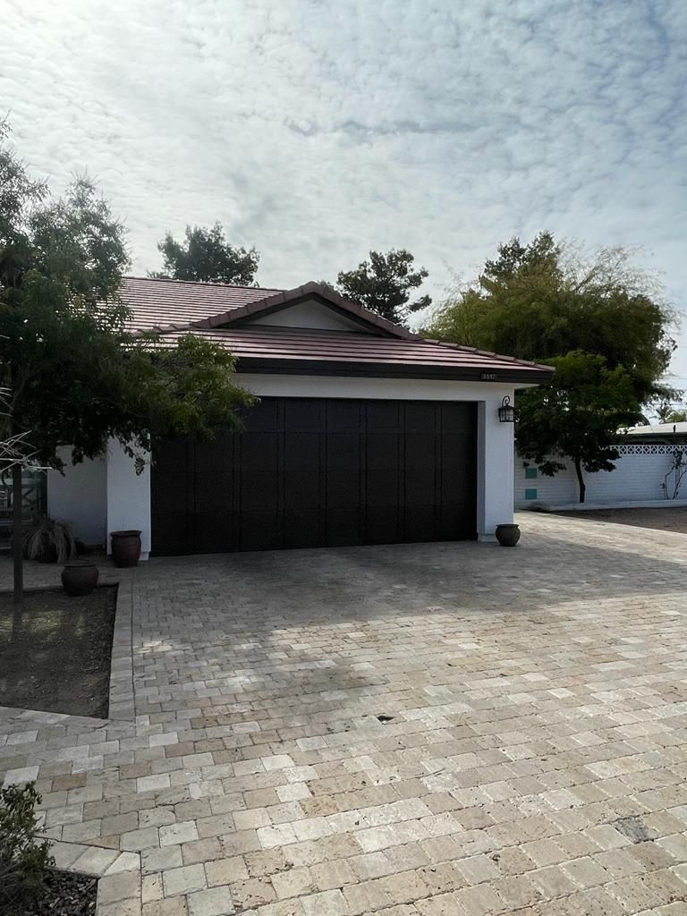 A detached garage with a dark brown door, red tile roof, and brick driveway.