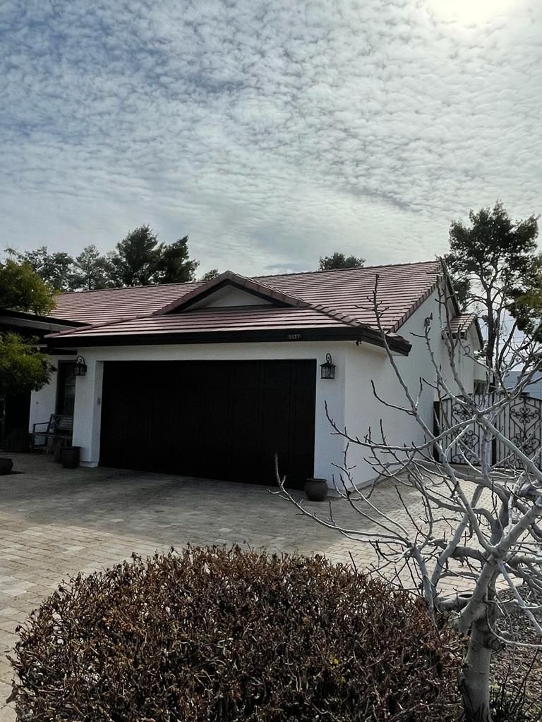 White house with a brown garage door and reddish roof, under a cloudy sky.