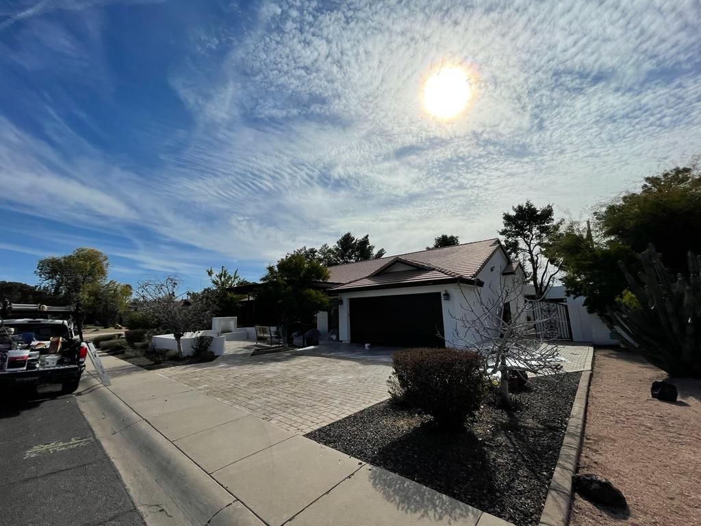 House with a dark garage door under a bright sun, with blue sky and streaky clouds.