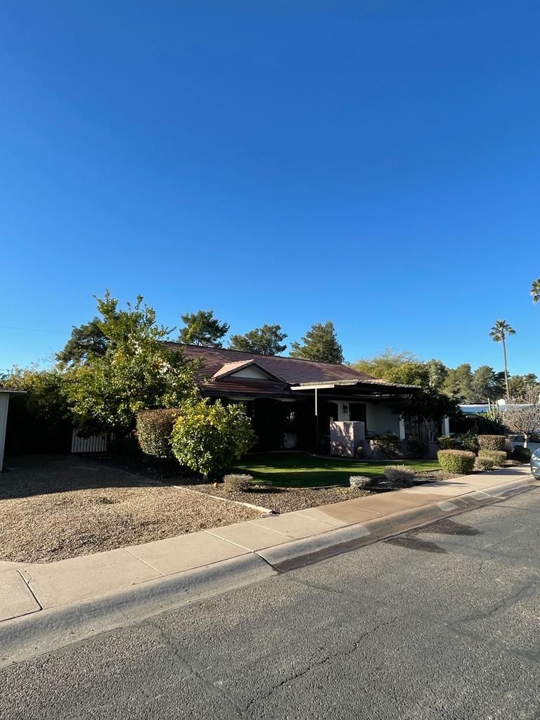 House with brown roof, front yard with green bushes and grass, clear blue sky.
