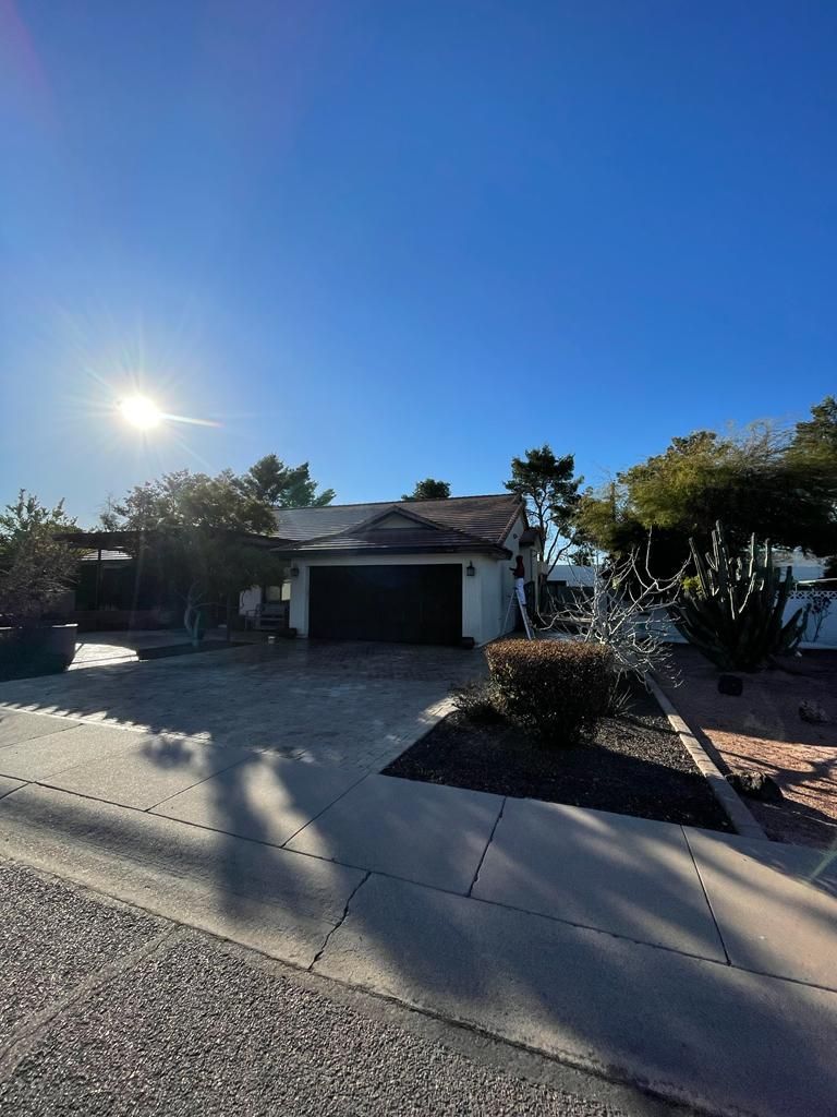 Residential home with a dark garage door, bright sunlight, and clear blue sky.