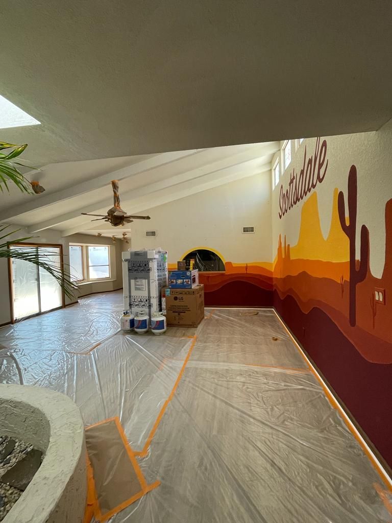 Interior with desert mural, plastic sheeting, painting supplies, and skylight.