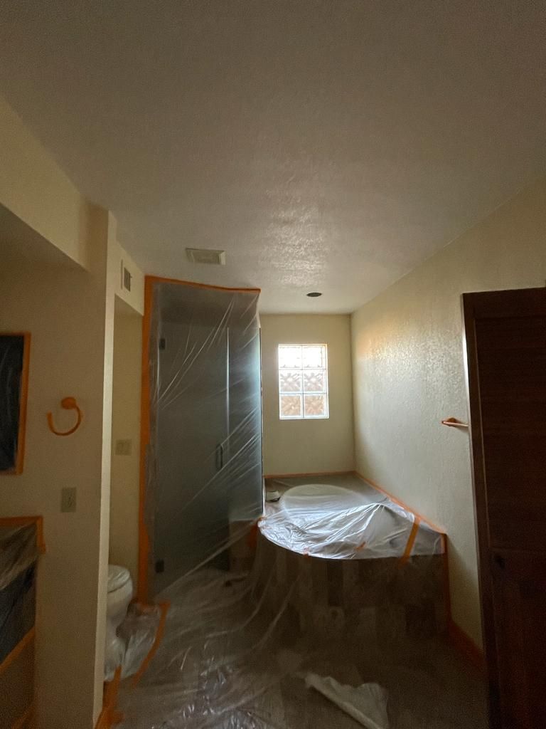 Bathroom under construction; shower, tub, toilet, and doorway covered in plastic; tan walls.