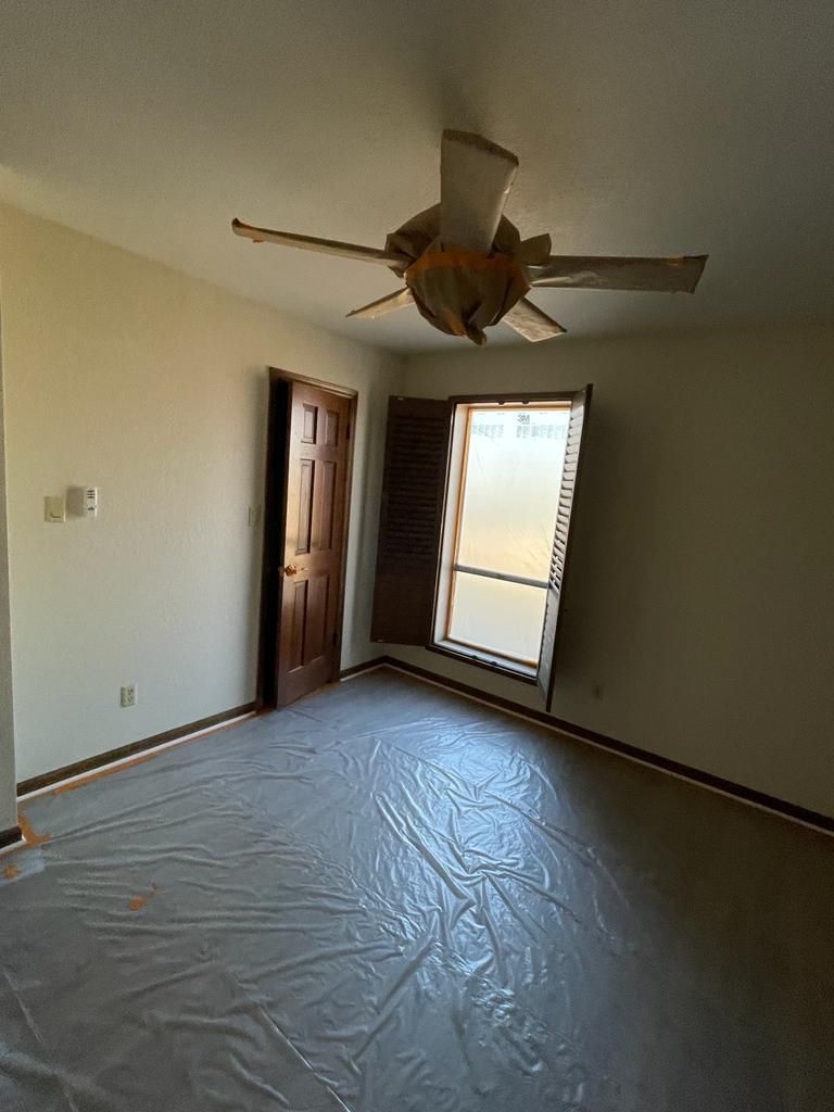 Empty room with window, door, and ceiling fan; plastic covers the floor.