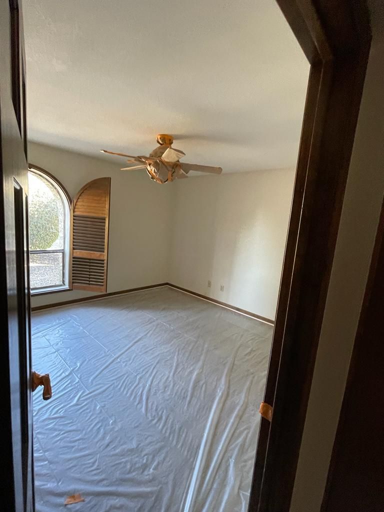 Empty room with plastic covering the floor, arched window, ceiling fan, and wooden doorframe.