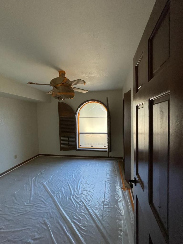 Empty room with arched window, ceiling fan, plastic-covered floor, and a closed wooden door.