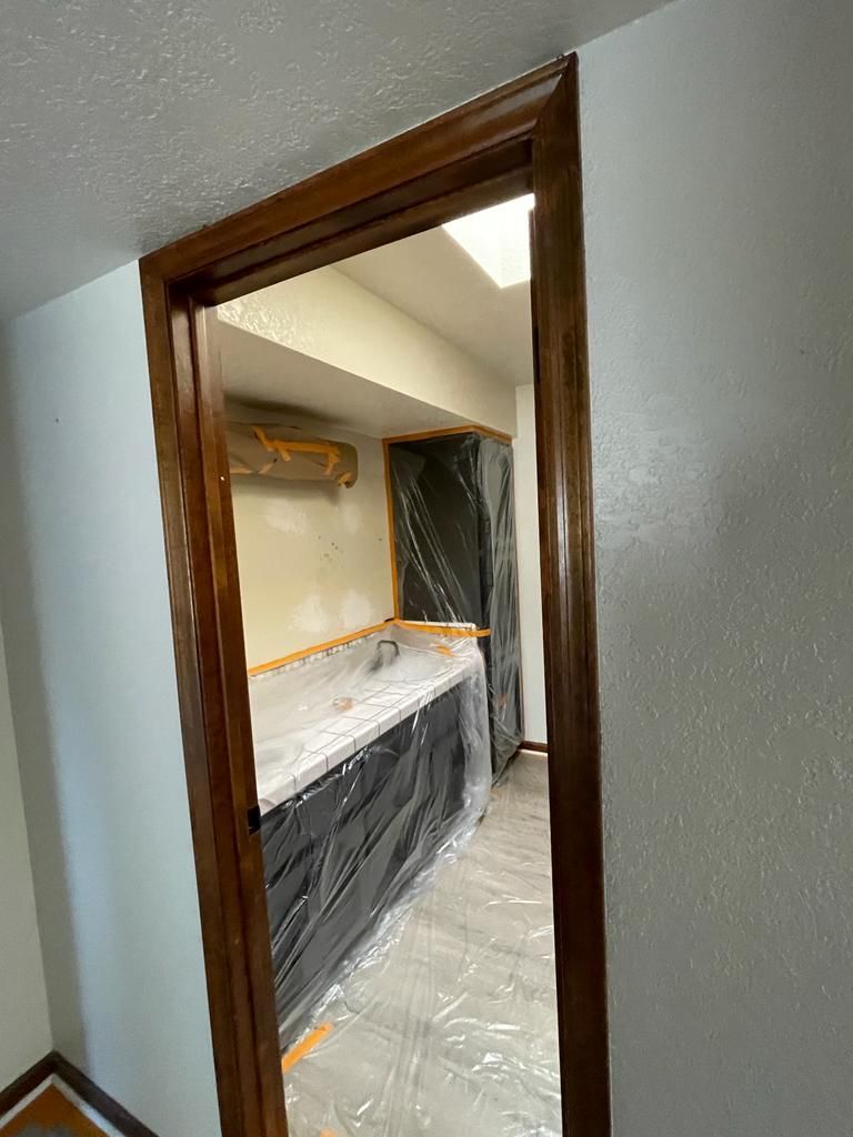 Wooden door frame leading into a kitchen being renovated; countertops covered in plastic.