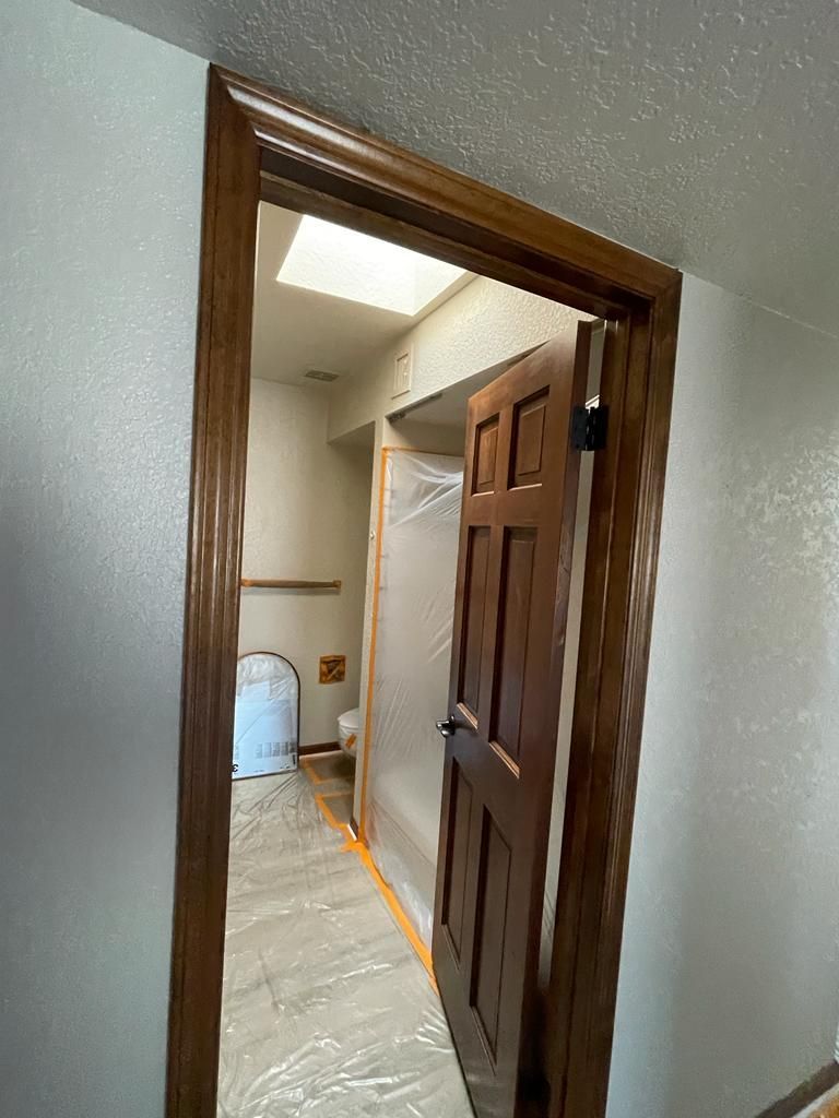Open wooden door with brown trim, leading to a room covered in plastic. A skylight is visible above.