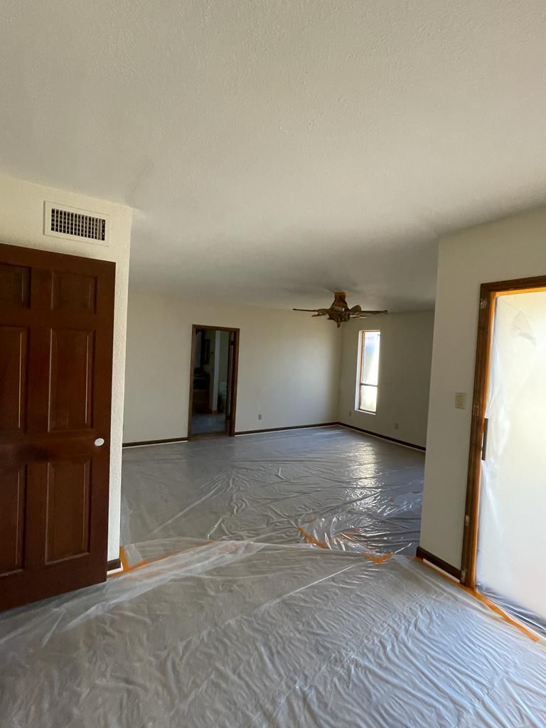 Interior room with protective plastic on the floor; dark wooden door on left, doorways in the distance.