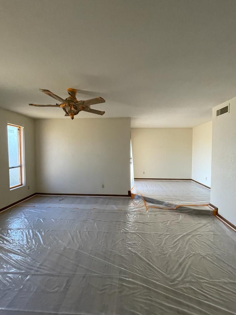 Empty room with protective plastic on the floor. Beige walls, a ceiling fan, and a doorway.