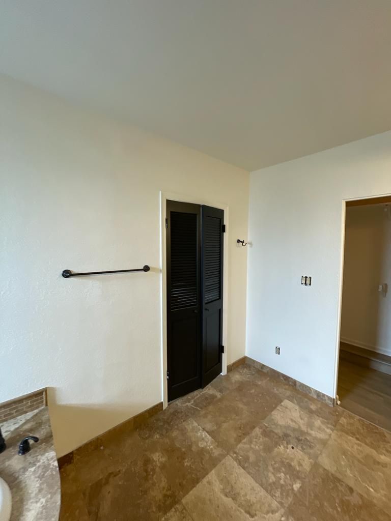 Bathroom with black shuttered door, tan tile floor, off-white walls, and a towel rack.