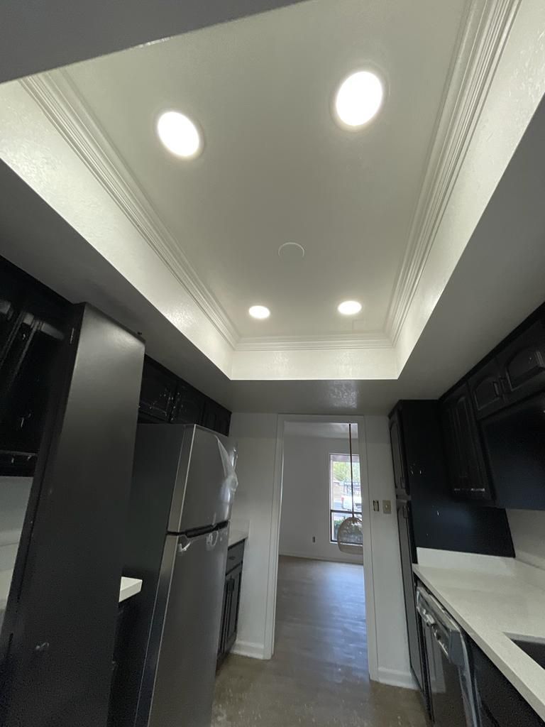 Kitchen with black cabinets, white countertops, recessed lighting, and a view into a hallway.