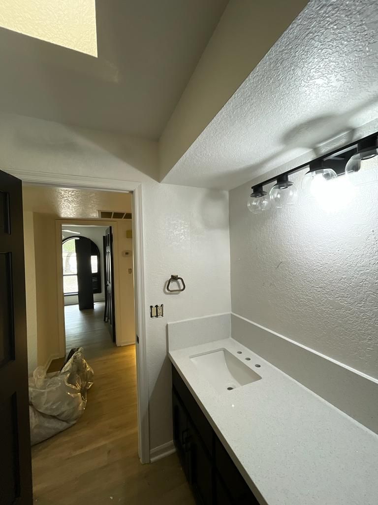 Bathroom with white countertop, dark cabinets, and textured walls.