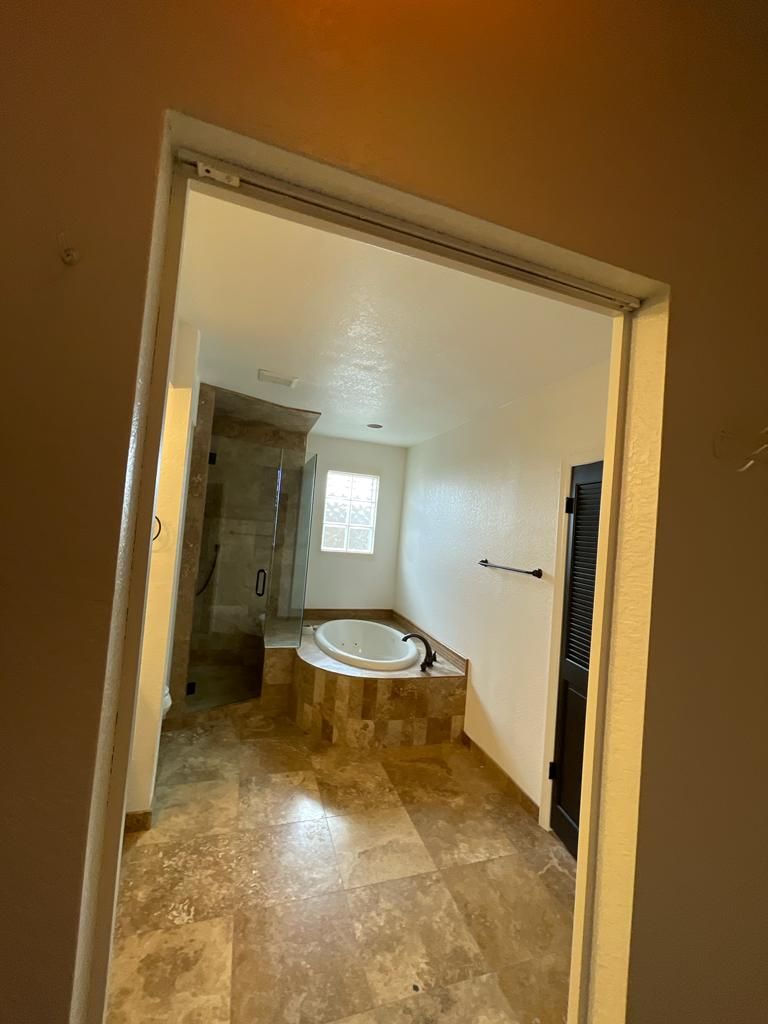 Bathroom interior with a raised bathtub, shower, and window. Beige tile floor and walls.