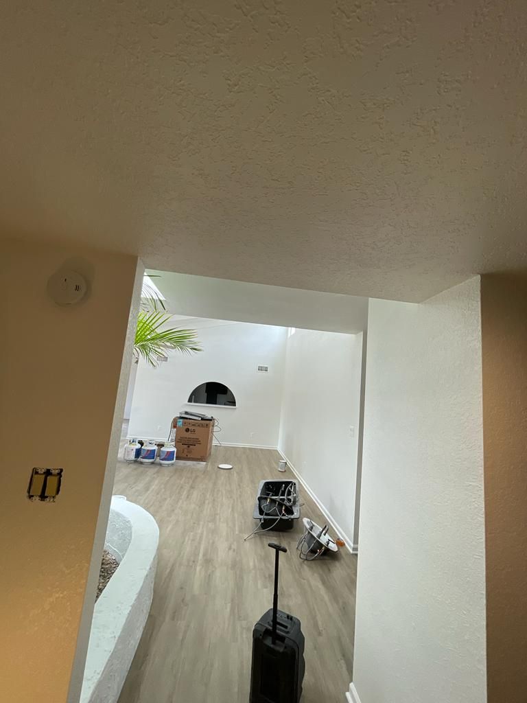 Interior view through a doorway with a high ceiling, hardwood floors, and construction materials.
