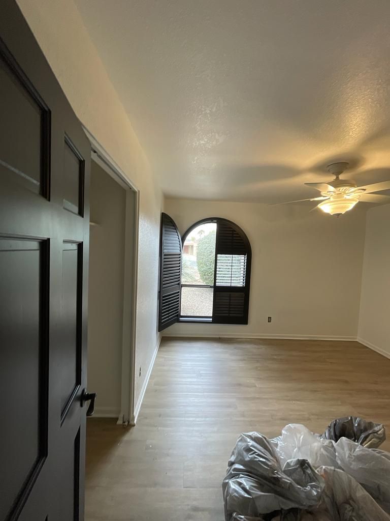 Interior of a room with hardwood floors, an arched window with shutters, and a dark door.