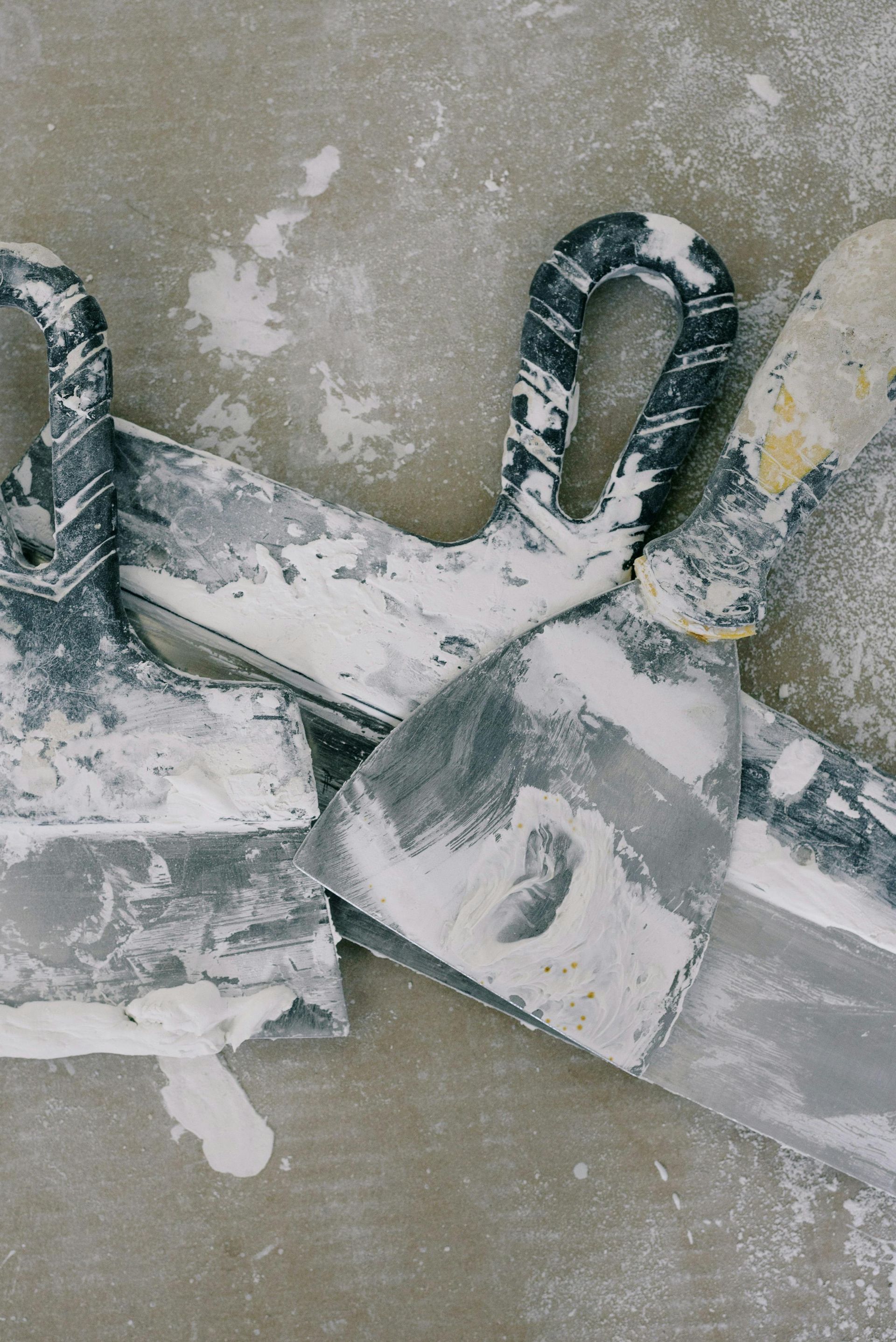 Three dusty putty knives on a light brown surface, covered in white drywall dust.