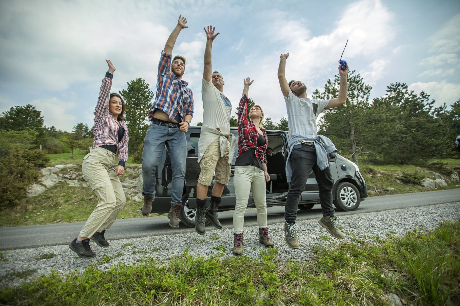 A group of people are jumping in the air in front of a car.