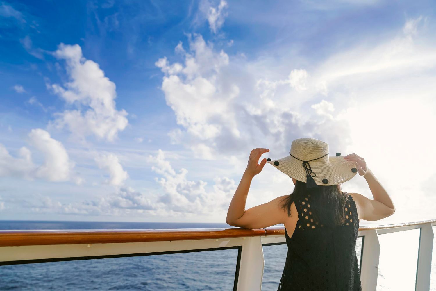 A woman is standing on a cruise ship looking out over the ocean.