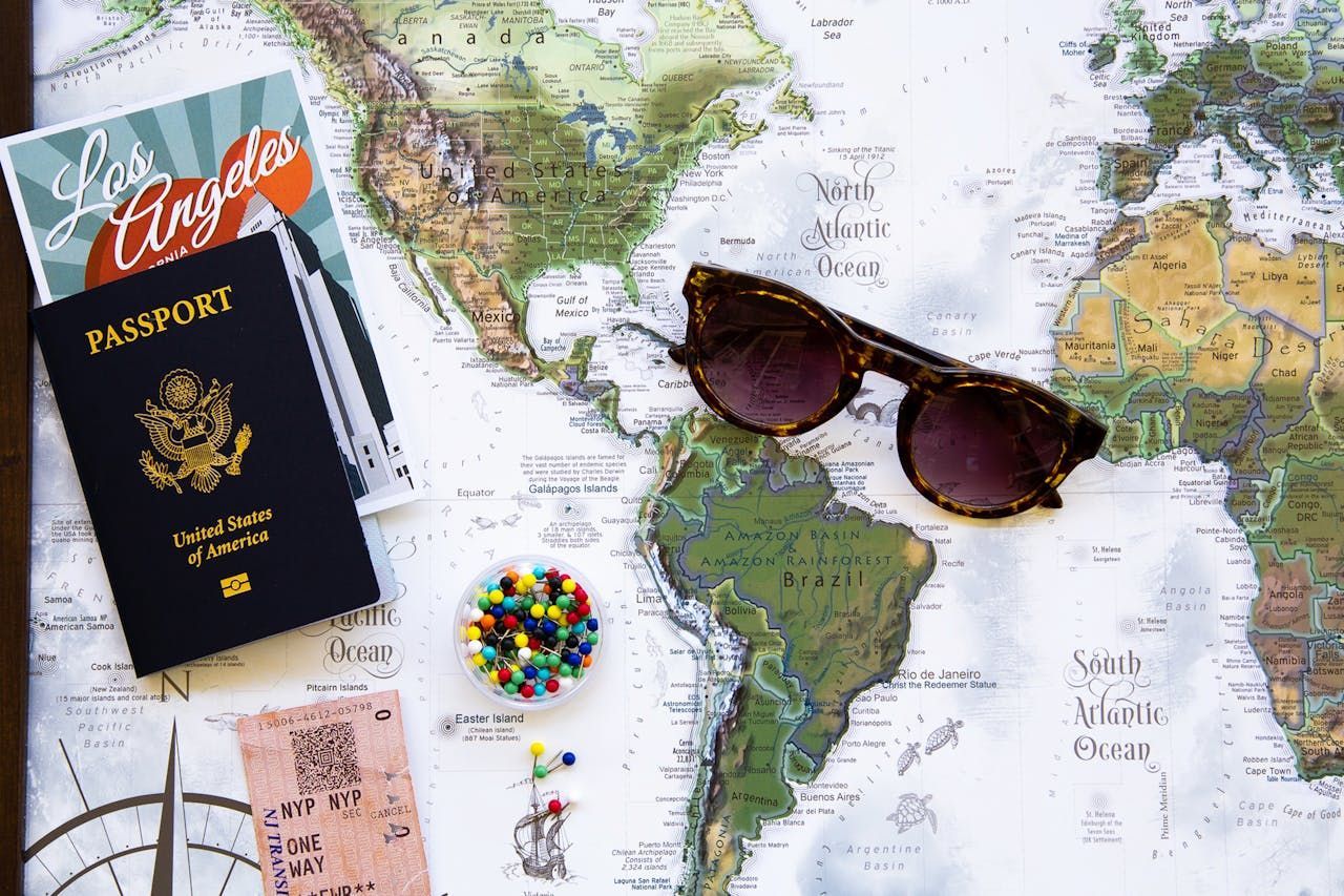 A passport , sunglasses , tickets , pins and a map on a table.