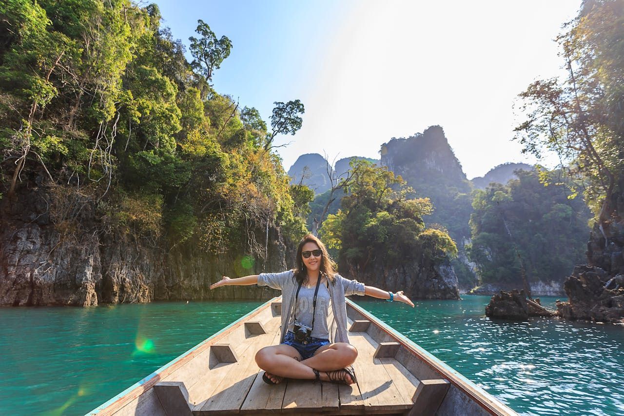 A woman is sitting in a boat on a lake with her arms outstretched.