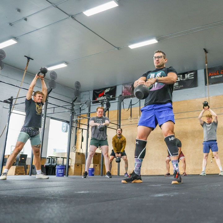 A group of people are doing exercises in a gym with a sign on the wall that says rogue