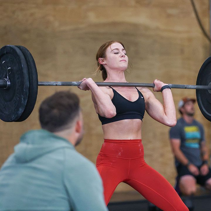 A woman is lifting a barbell over her head while a man watches.